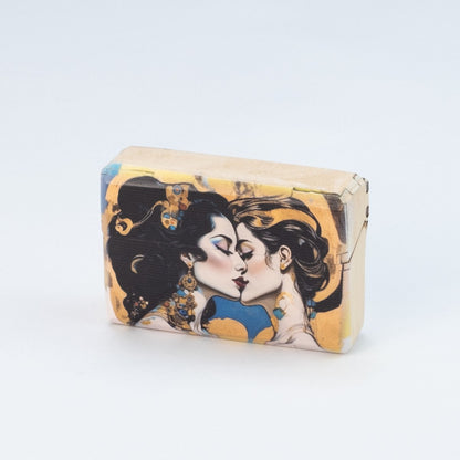 Auf dem Bild ist ein Etui für E-Zigaretten zu sehen. Darauf gemalt sind zwei Frauen mit langen Haaren und Goldschmuck, die sich küssen. Es ist ein Etui von Nuf-Nuf, aus nachhaltigem Holz, handgefertigt und hochqualitativ verarbeitet.